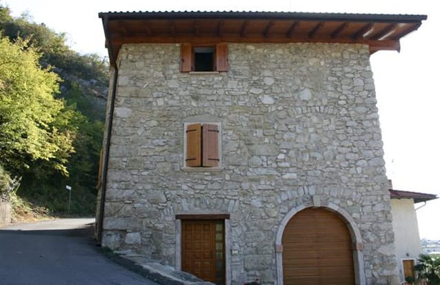 Casa in pietra con garage e finestre in legno, vista su strada e natura.