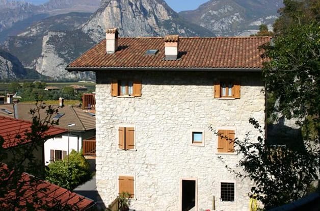 Casa di civile abitazione in pietra con tetto in terracotta e finestre con persiane in legno.