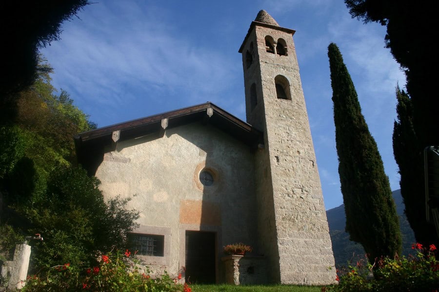 Chiesa di San Siro con campanile in pietra e vegetazione circostante.