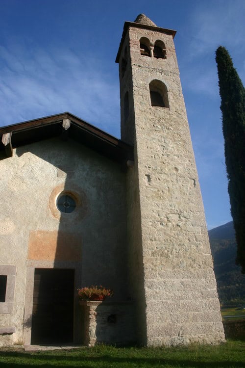 Campanile storico della Chiesa di San Siro con cielo azzurro e cipressi.
