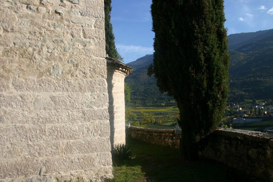 Vista della chiesa di San Siro con pareti in pietra e paesaggio montano sullo sfondo.