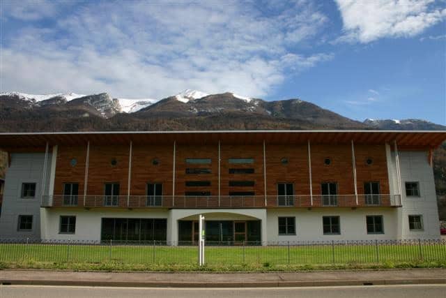 Edificio moderno in legno e cemento con montagne sullo sfondo.