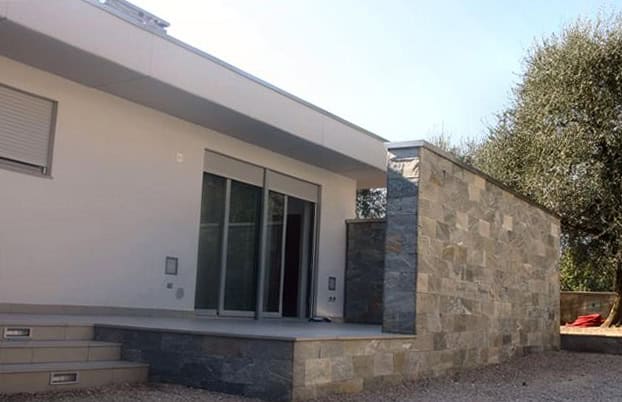 Casa moderna con parete in pietra e grandi porte scorrevoli in vetro.