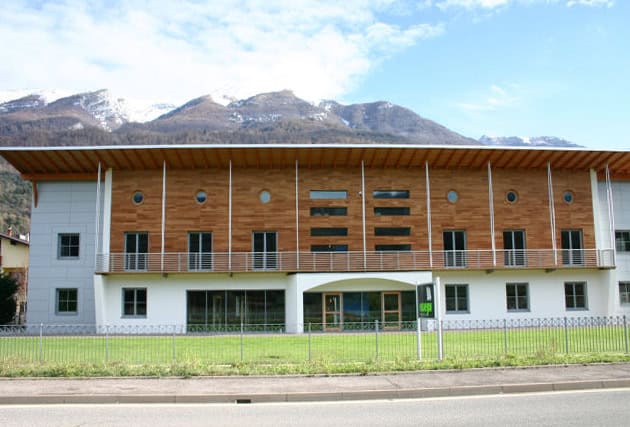 Edificio moderno con facciata in legno e balconi, situato in un'area panoramica montuosa.