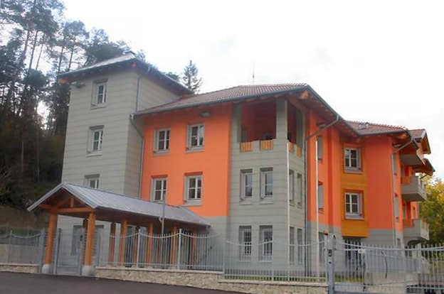 Edificio residenziale in costruzione con facciata arancione e grigia, vicino a un'area boschiva.