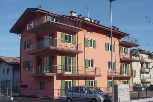 Edificio residenziale a tre piani con balconi e facciata rosa e verde.