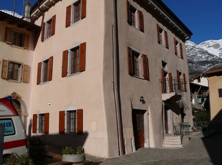 Edificio storico a Canonica Vezzano con finestre in legno e montagne sullo sfondo.