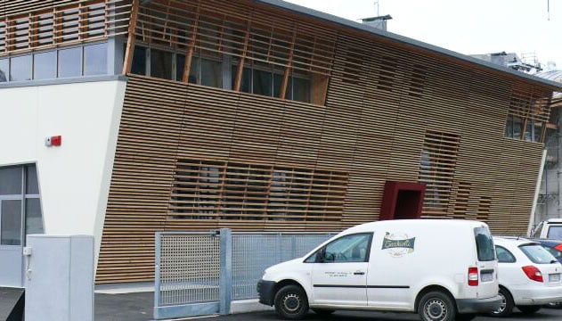 Edificio moderno con facciata in legno e veicoli in primo piano.