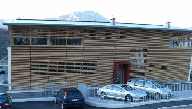 Edificio moderno in legno con parcheggio e montagne sullo sfondo.