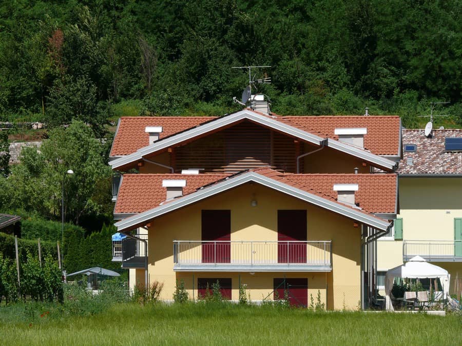 Casa di civile abitazione con tetto a falde rosso e balcone in zona verde.