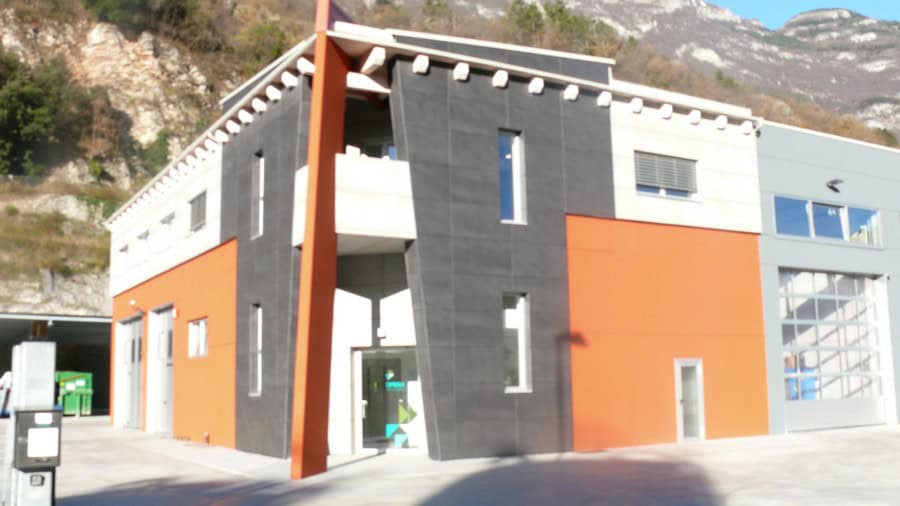 Edificio moderno con facciata in colori arancione e grigia, situato in zona montuosa.