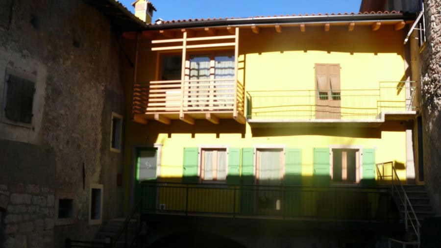 Edificio residenziale a Lasino con facciata gialla e balcone in legno.