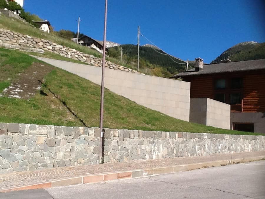 Costruzioni Dallapè Srl lavori di edilizia in zona montana con muro in pietra e case in legno.