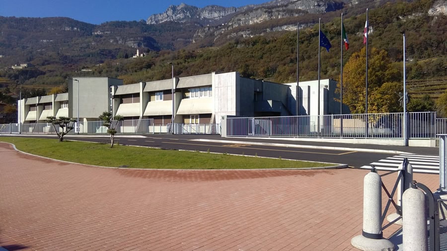 Edificio moderno con bandiere e montagne sullo sfondo, costruzione Dallapè Srl.