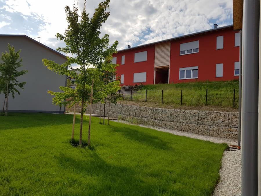 Edificio residenziale moderno con giardino ben curato e alberi.