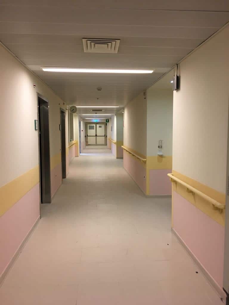 Corridor ospedaliero con pareti colorate e illuminazione moderna.