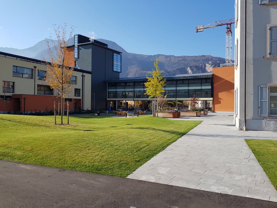 Edificio moderno con giardino e montagne sullo sfondo, costruzione Dallapè Srl.