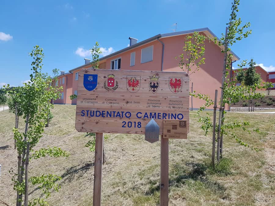 Segnale di benvenuto a Studentato UNICAM Camerino con edificio in background.