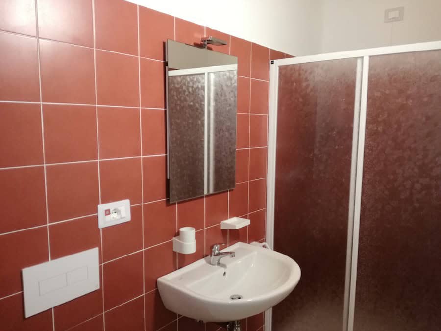 Bagno con piastrelle rosse, lavabo e specchio.