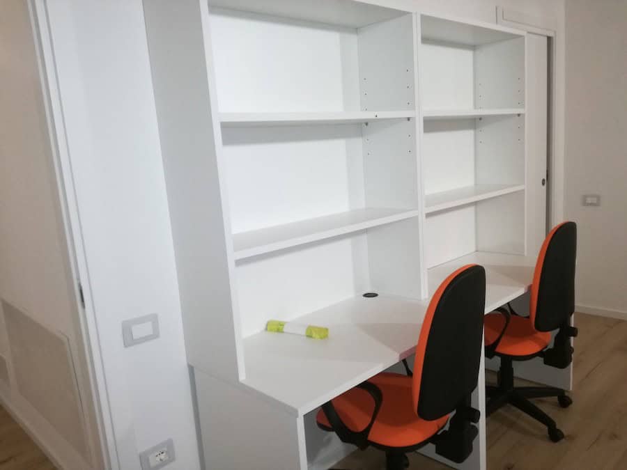 Scrivania con libreria bianca e sedie arancioni in ufficio moderno.