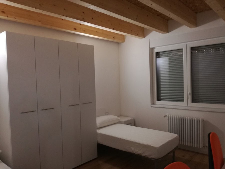 Camera da letto moderna con armadio bianco e finestra con tapparelle.