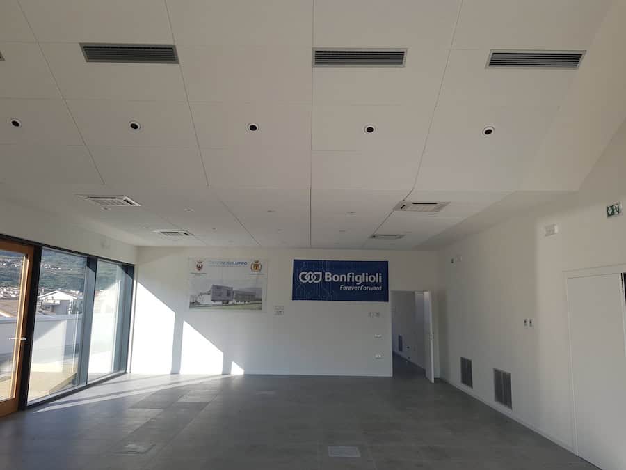Interno di un capannone industriale con grandi finestre e pannelli acustici sul soffitto.