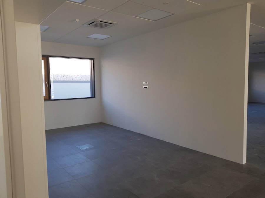 Interno di capannone industriale con pareti bianche e finestra.