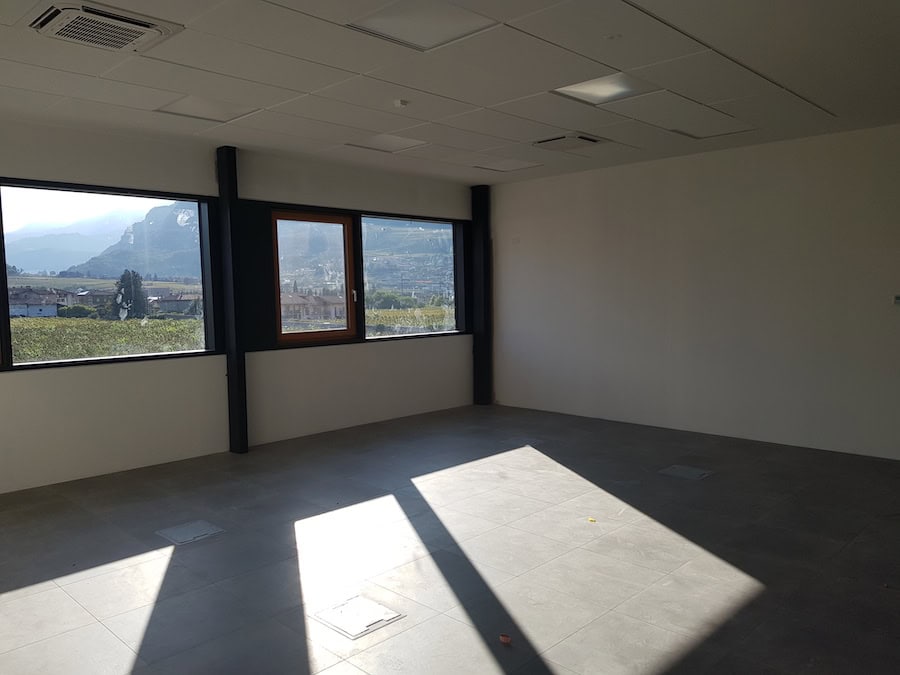 Interno ufficio con grandi finestre e vista sulle montagne.