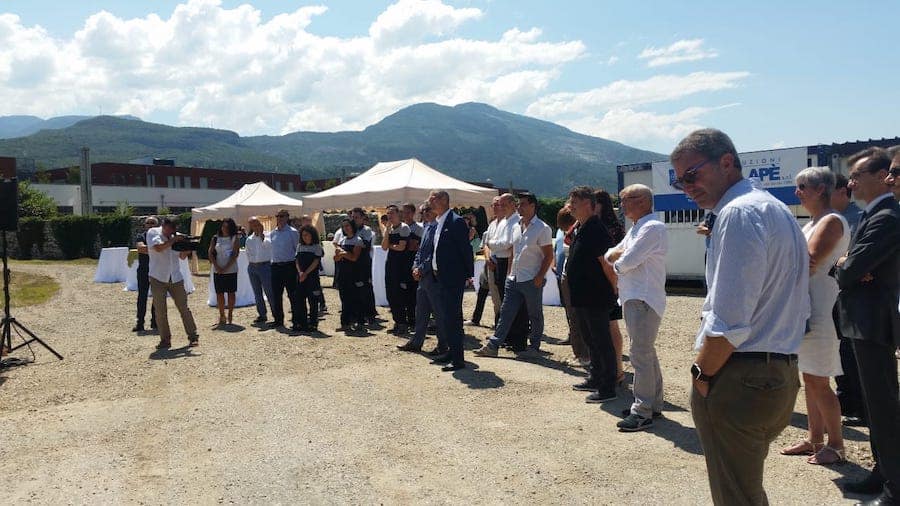 Gruppo di persone in un evento all'aperto vicino a un capannone industriale.