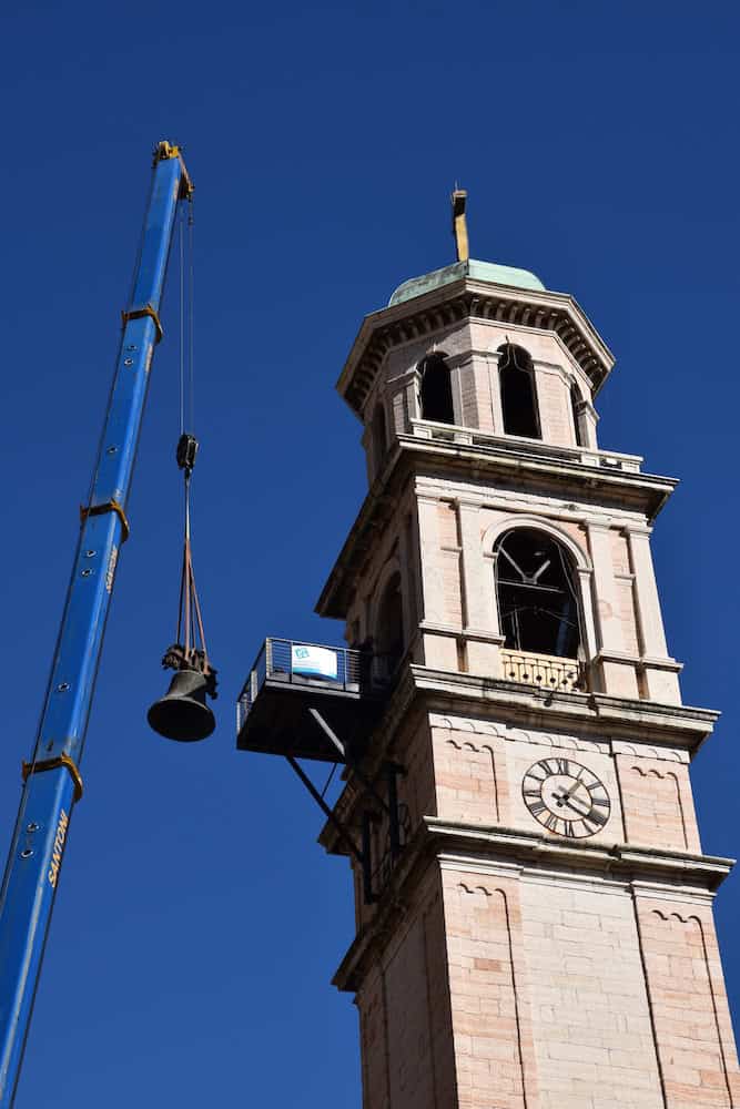 Lavori di restauro sulla torre della Chiesa di Aldeno con gru e piattaforma elevatrice.
