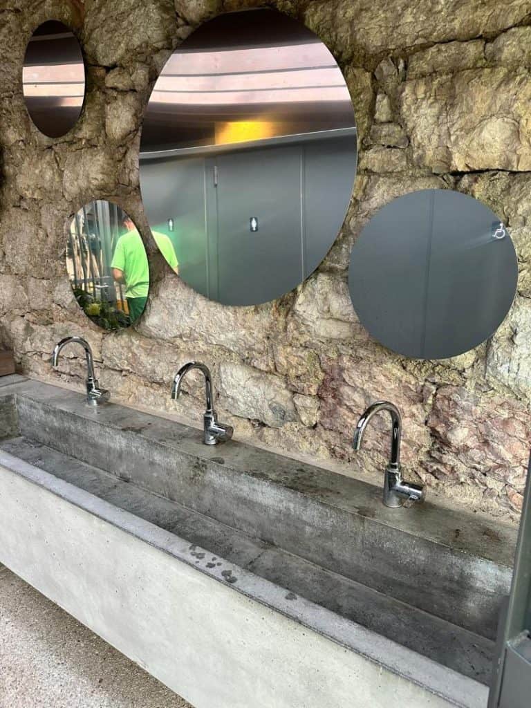 Lavandino pubblico con specchi rotondi in pietra naturale.