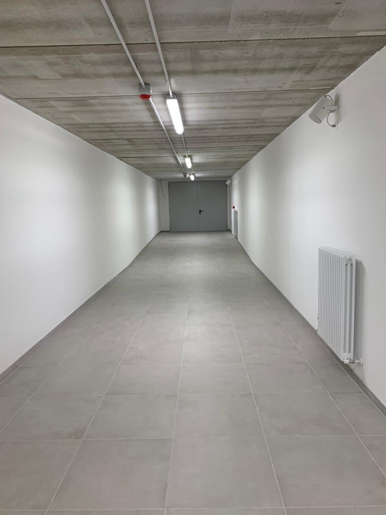 Corridor interno con pareti bianche e soffitto in cemento a vista.