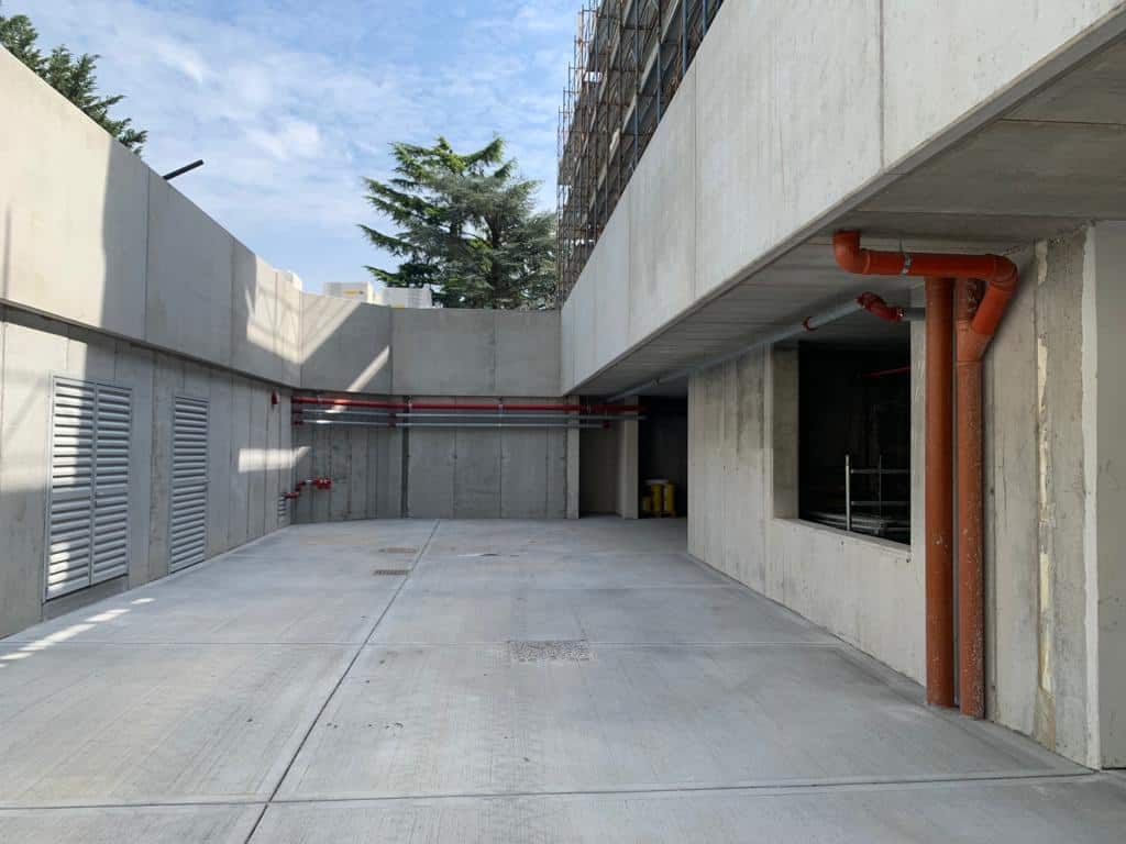 Area esterna di un edificio in costruzione con tubature visibili e pareti di cemento.