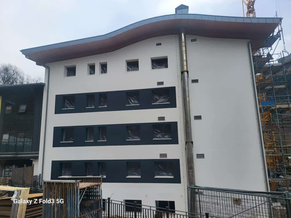 Edificio in costruzione con facciata bianca e finestre nere, in fase di ristrutturazione.